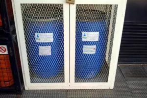 Bidones azules almacenados en armario metálico con rejilla
