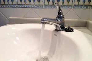 Grifo abierto con agua corriendo en lavabo blanco
